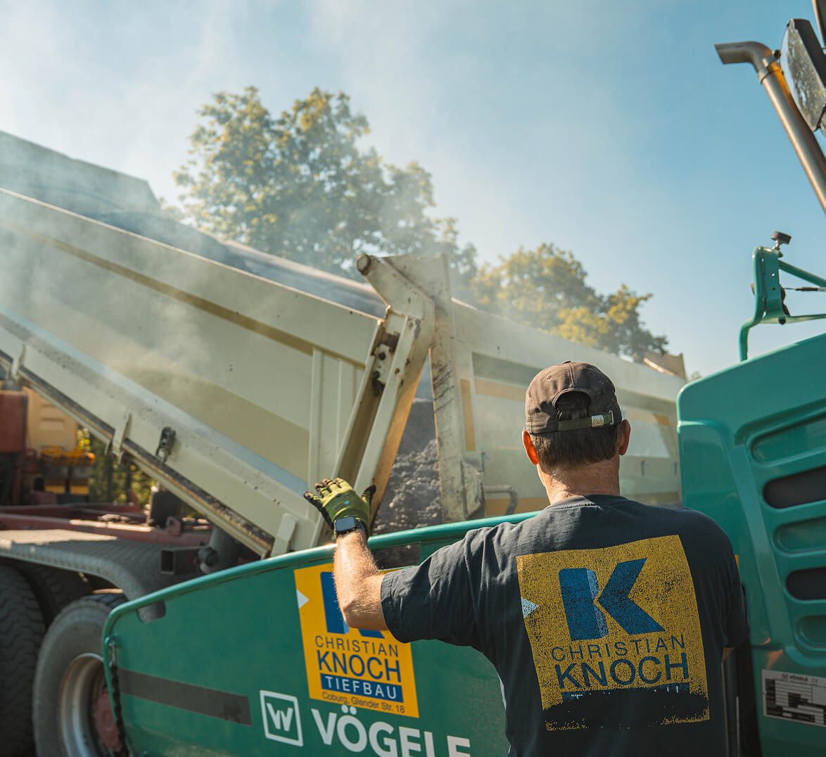 Mitarbeiter von Christian Knoch Tiefbau beim Einbau von Asphalt mit Straßenfertiger und Kipper auf einer Straßenbaustelle.