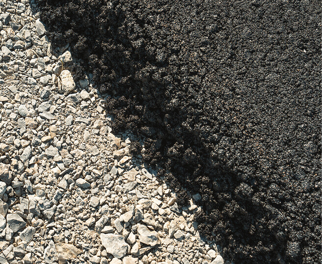 Frisch aufgetragener Asphalt auf Schotterunterbau beim Straßenbau