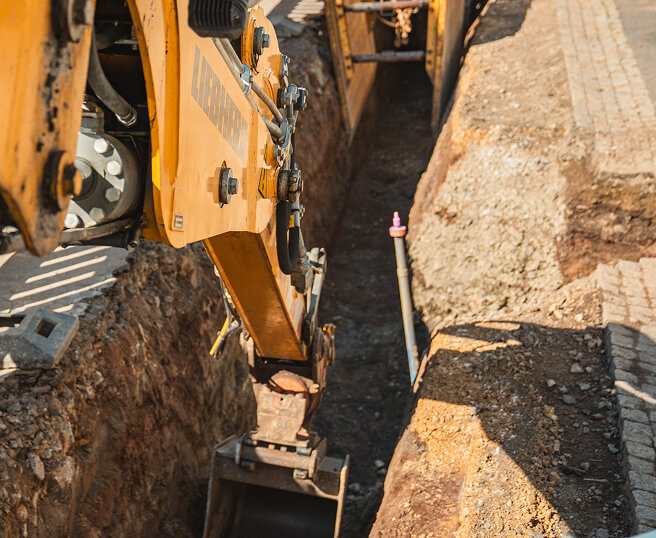Bagger beim Ausheben eines Leitungsgrabens auf einer Tiefbaustelle.