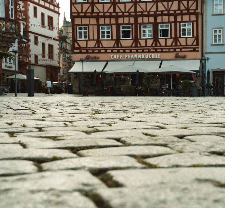 Aufnahme des historischen Kopfsteinpflasters auf dem Coburger Marktplatz mit Fachwerkhäusern und Gastronomie im Hintergrund – Referenzprojekt von Christian Knoch Tiefbau.