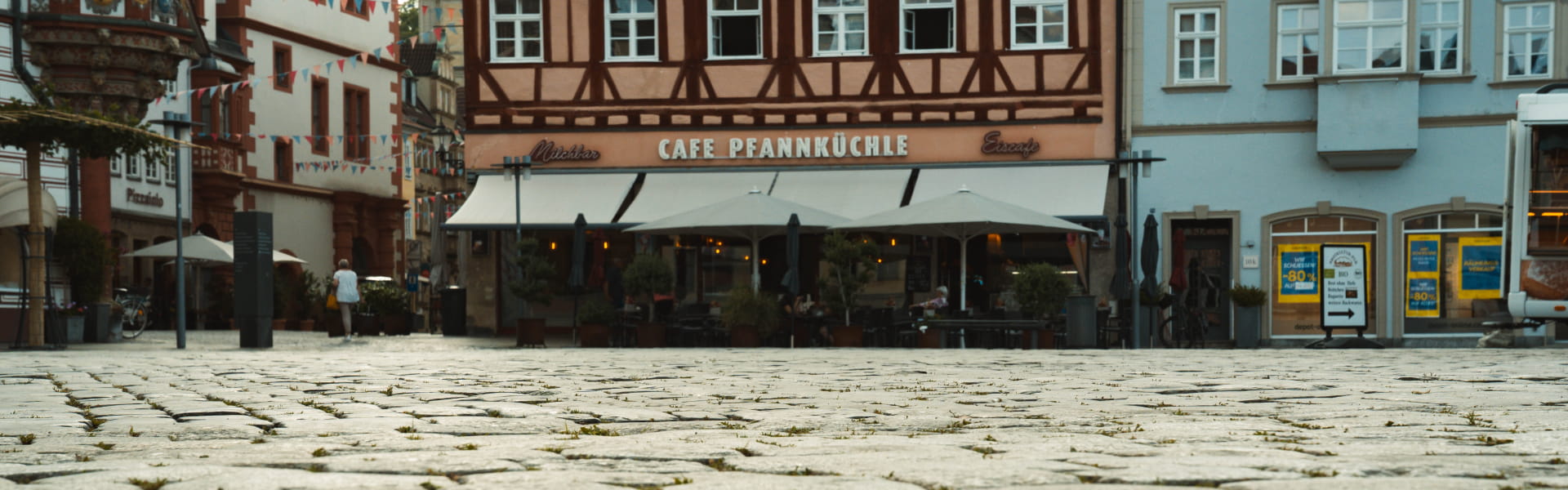 Panoramaaufnahme des historischen Kopfsteinpflasters auf dem Coburger Marktplatz mit Fachwerkhäusern und Gastronomie im Hintergrund – Referenzprojekt von Christian Knoch Tiefbau.