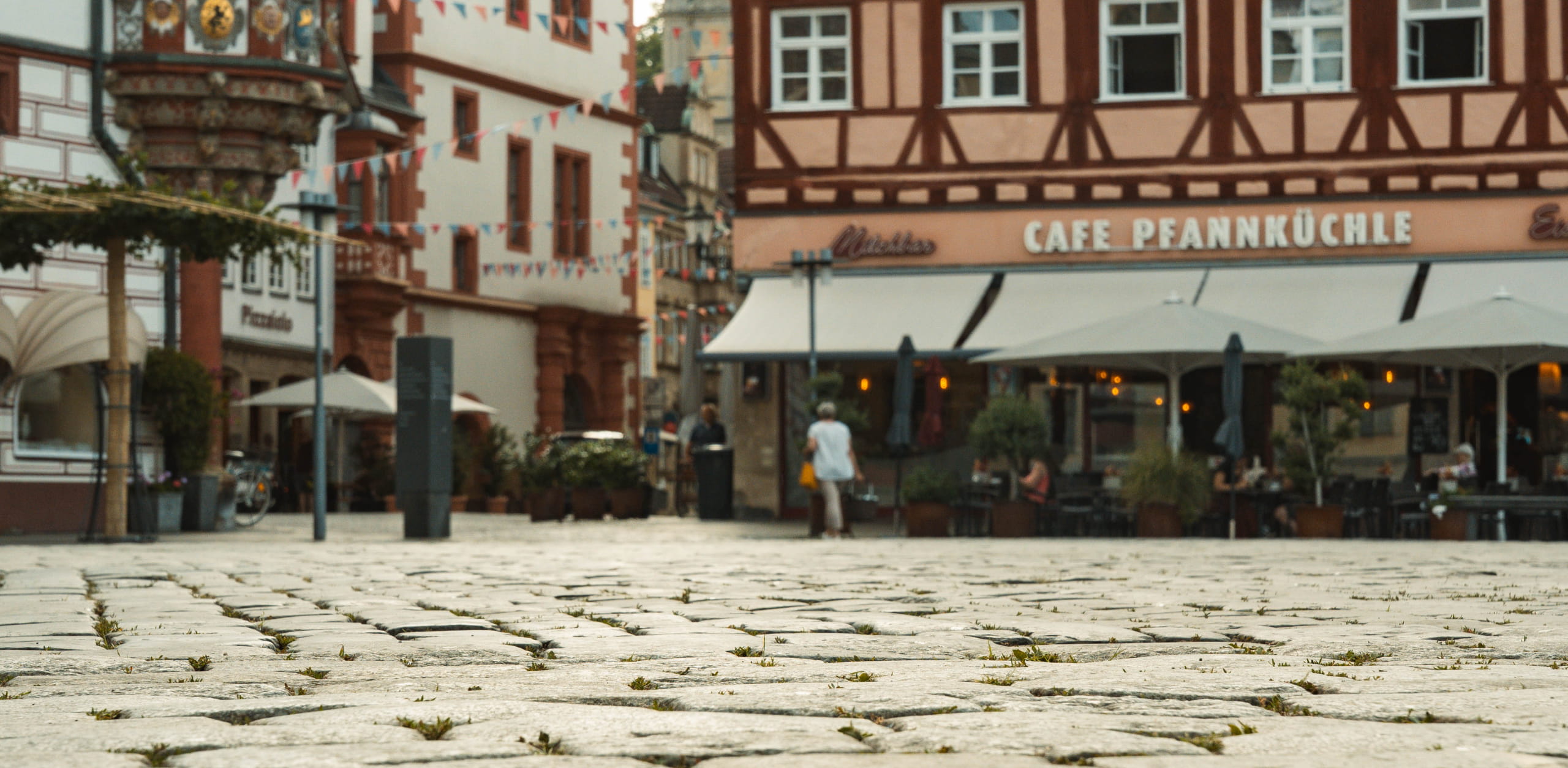 Bodentiefe Aufnahme des historischen Kopfsteinpflasters auf dem Coburger Marktplatz mit Fachwerkhäusern und Gastronomie im Hintergrund – Referenzprojekt von Christian Knoch Tiefbau.
