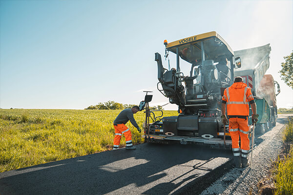 Straßenbauarbeiter bedienen einen Asphaltfertiger beim Einbau einer neuen Fahrbahndecke.