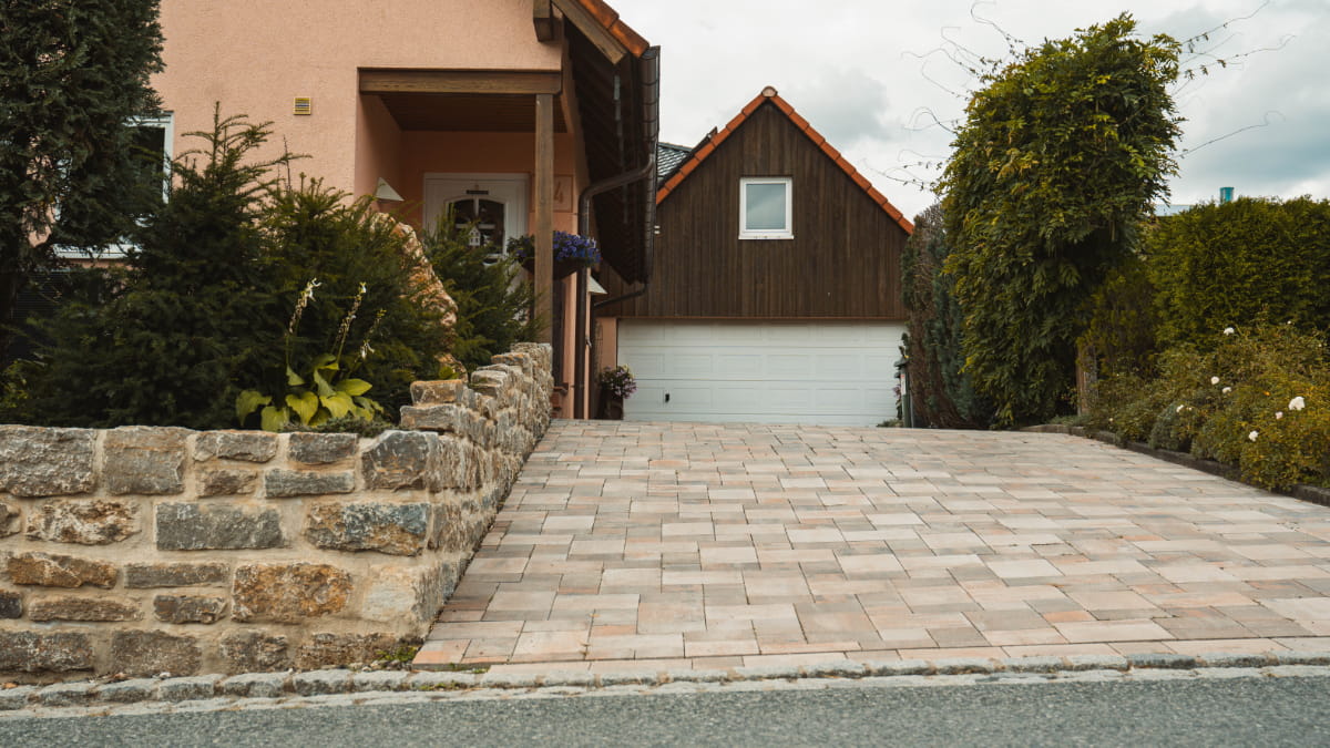 Gepflasterte, beheizte Hofeinfahrt vor einer Garage mit angrenzender Natursteinmauer und Gartenbepflanzung.