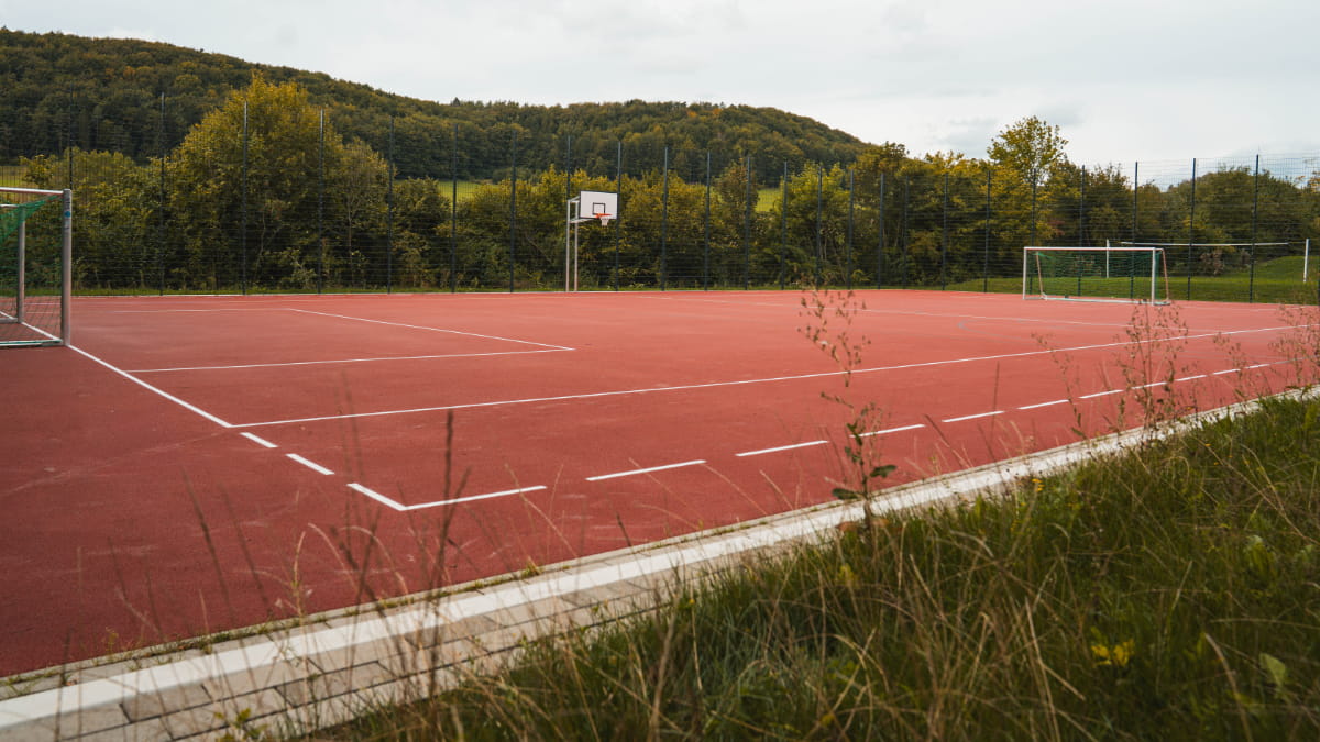 Roter Multifunktions-Sportplatz mit Fußballtoren und Basketballkorb an der Jugendbildungsstätte Neukirchen.