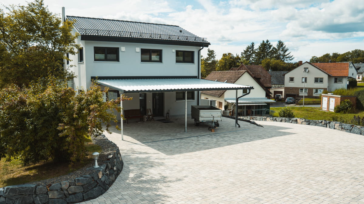 Großzügig gepflasterte Hoffläche vor einem Wohnhaus mit Carport und geschwungener Natursteinmauer.