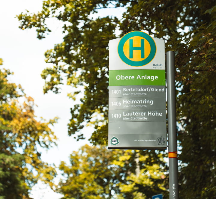 Haltestellenschild „Obere Anlage“ in Coburg mit Bäumen.