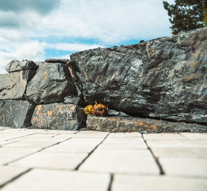 Detailansicht einer Natursteinmauer entlang einer hell gepflasterten Hoffläche.