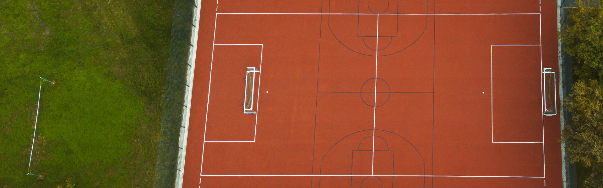 Luftaufnahme eines roten Multifunktions-Sportplatzes mit Fußballtoren und Spielfeldmarkierungen an der Jugendbildungsstätte Neukirchen.
