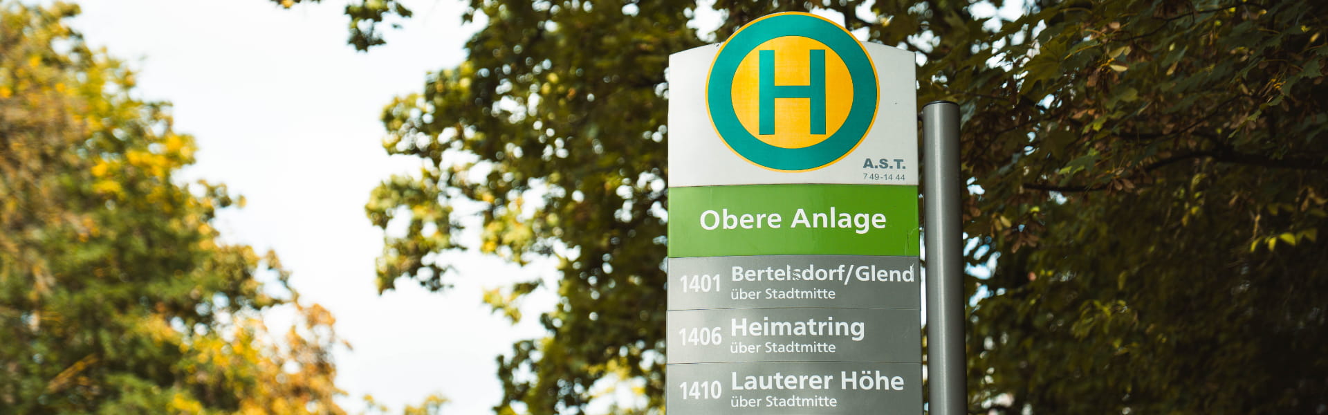Haltestellenschild „Obere Anlage“ in Coburg mit Bäumen.