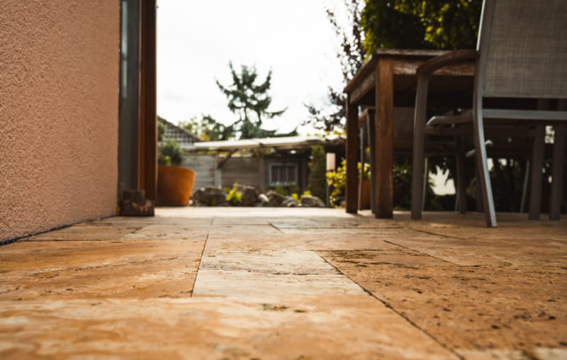 Gepflasterte Terrasse mit Natursteinplatten und Sitzmöbeln im Garten.