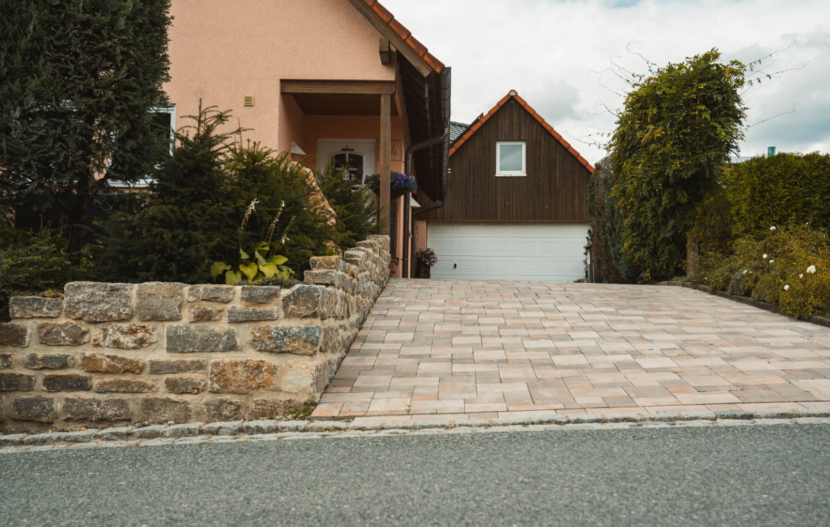 Gepflasterte, beheizte Hofeinfahrt vor einer Garage mit seitlicher Natursteinmauer und Gartenbepflanzung.