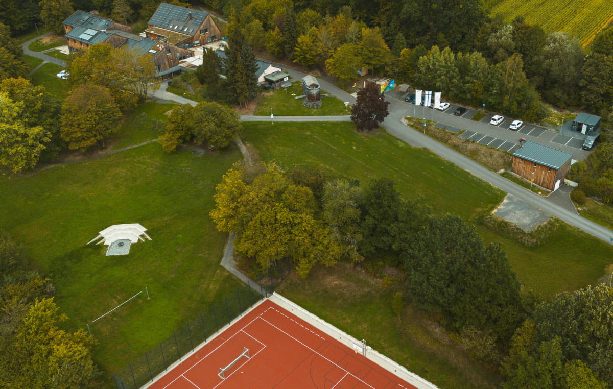 Luftaufnahme der Jugendbildungsstätte Neukirchen mit Sportplatz, Grünflächen, Gebäuden und Parkplatz.