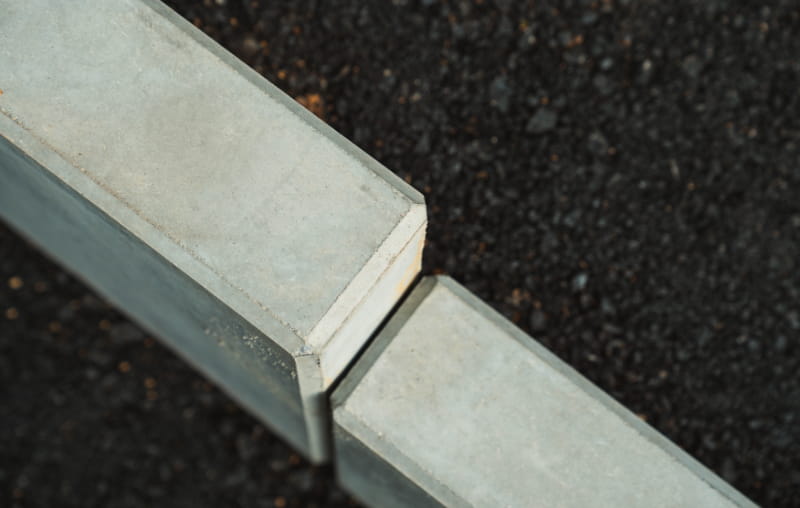 Detailansicht zweier hellgrauer Bordsteine mit schmaler Fuge auf dunklem Asphalt.