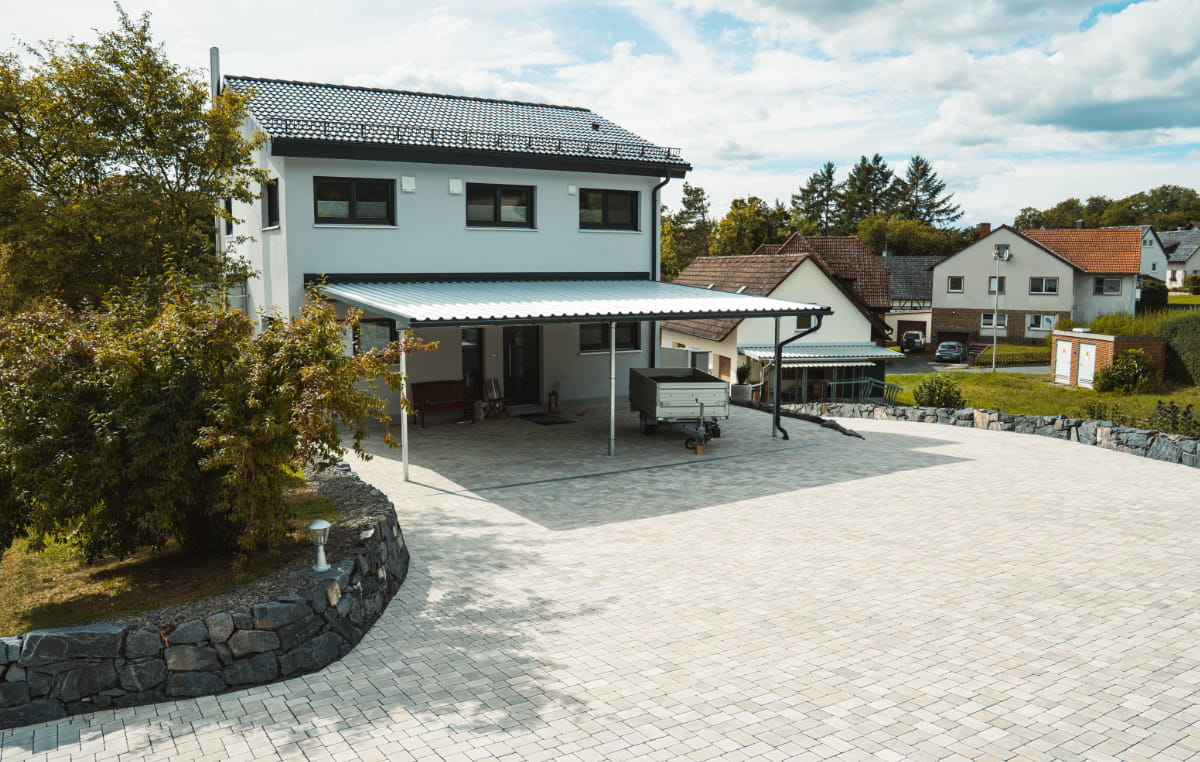Großzügig gepflasterte Hoffläche vor einem Wohnhaus mit Carport und geschwungener Natursteinmauer.