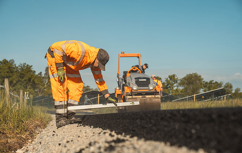 Mitarbeiter kontrolliert die Einbauhöhe der Asphalt-Tragdeckschicht während der Sanierung des Wirtschaftswegs.